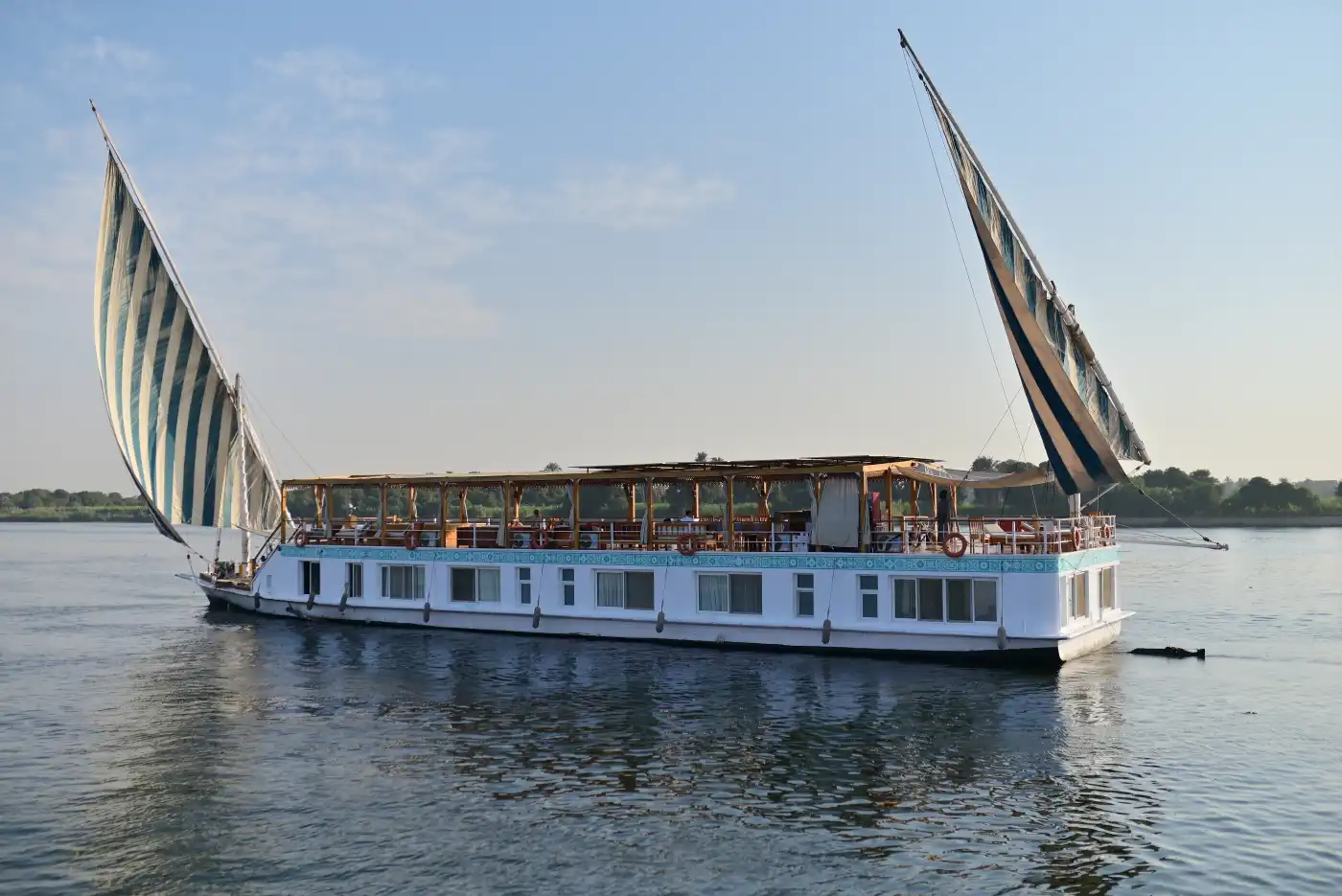 Golden Horizons | Croisière Dahabiya 14 Jours Turquoise Dahabiya naviguant sur le Nil avec les voiles entièrement levées